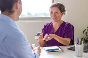 Profissional de saúde do sexo feminino mostrando um medidor de glicose e um dispositivo de punção para uma paciente em consulta médica. Conceito de educação, diagnóstico e gestão da saúde em diabetes.