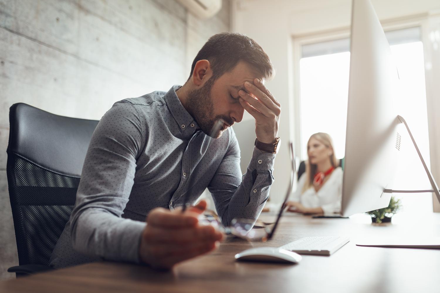 Stressed man at work, woman nearby.